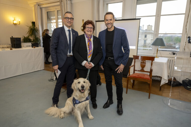 Décoration par Brigitte Klinket, Questeure, de TOBY 500e Chien d’Assistance à mission collective de l’Association Handi’Chiens présidée par M. Robert Kohler, à l'Assemblée nationale le 26 mars 2025.