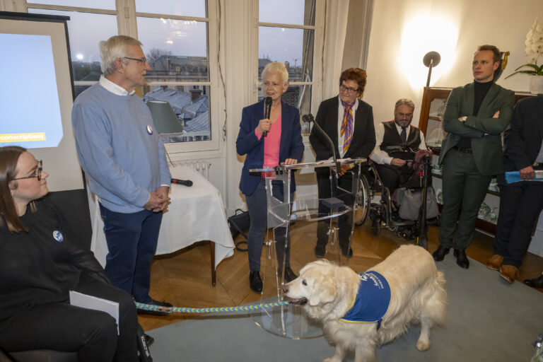 Décoration par Brigitte Klinket, Questeure, de TOBY 500e Chien d’Assistance à mission collective de l’Association Handi’Chiens présidée par M. Robert Kohler, à l'Assemblée nationale le 26 mars 2025.